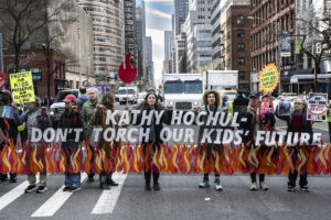 people holding banner with flames and text Kathy Hochul Don't Torch Our Kids' Future